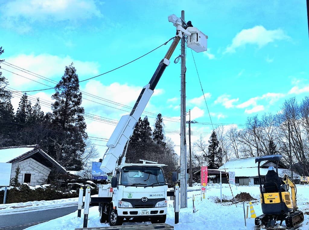 雪景色の中、高所作業車で電柱作業を行う株式会社コウクラフトの作業風景